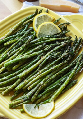 Roasted air fryer asparagus on a yellow square serving platter, garnished with lemon slices.