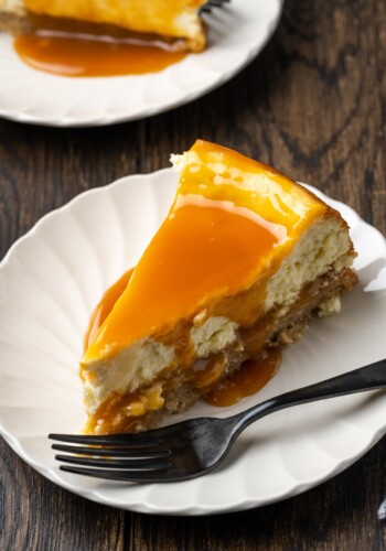 A slice of banana blondie cheesecake on a white plate with a fork, topped with salted caramel.