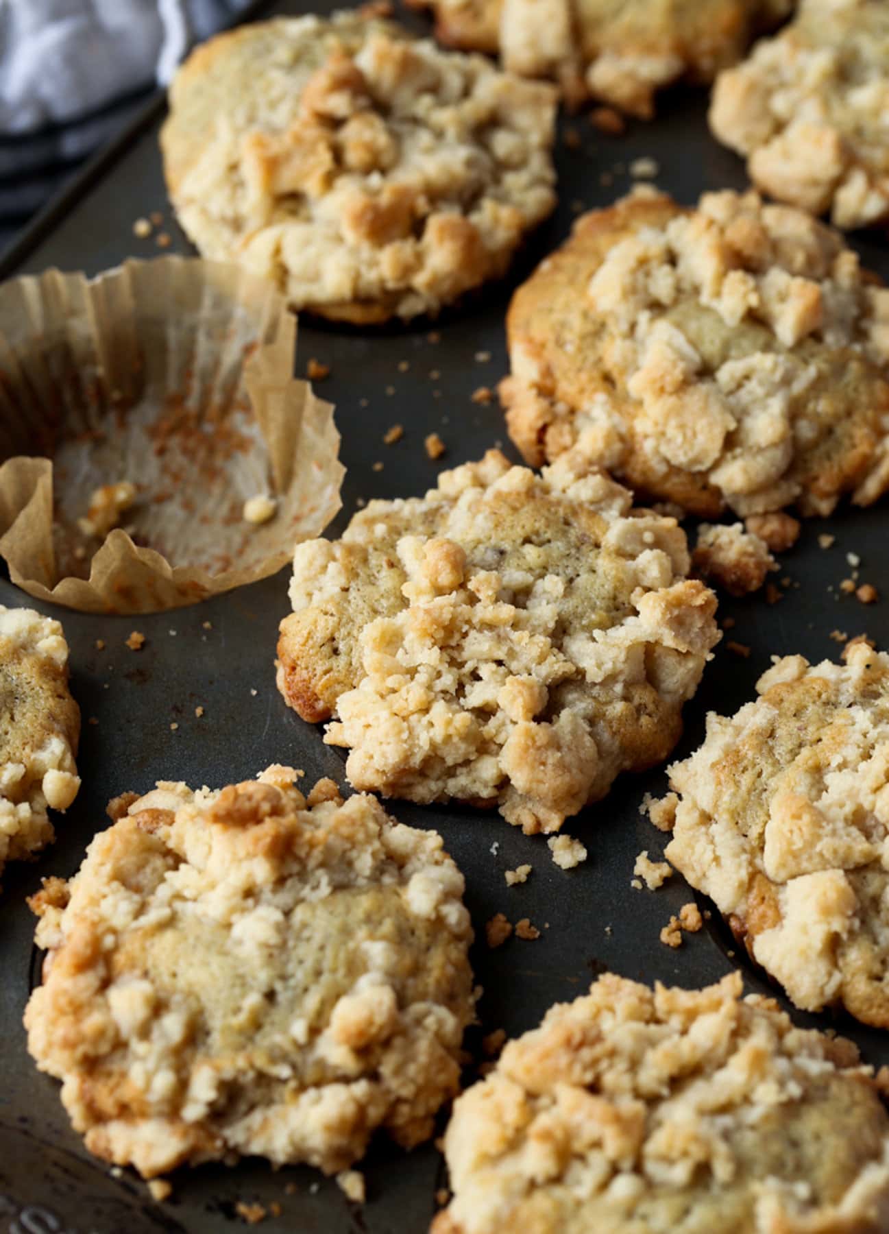 Banana Muffins with crumb topping in a muffin pan with one empty liner