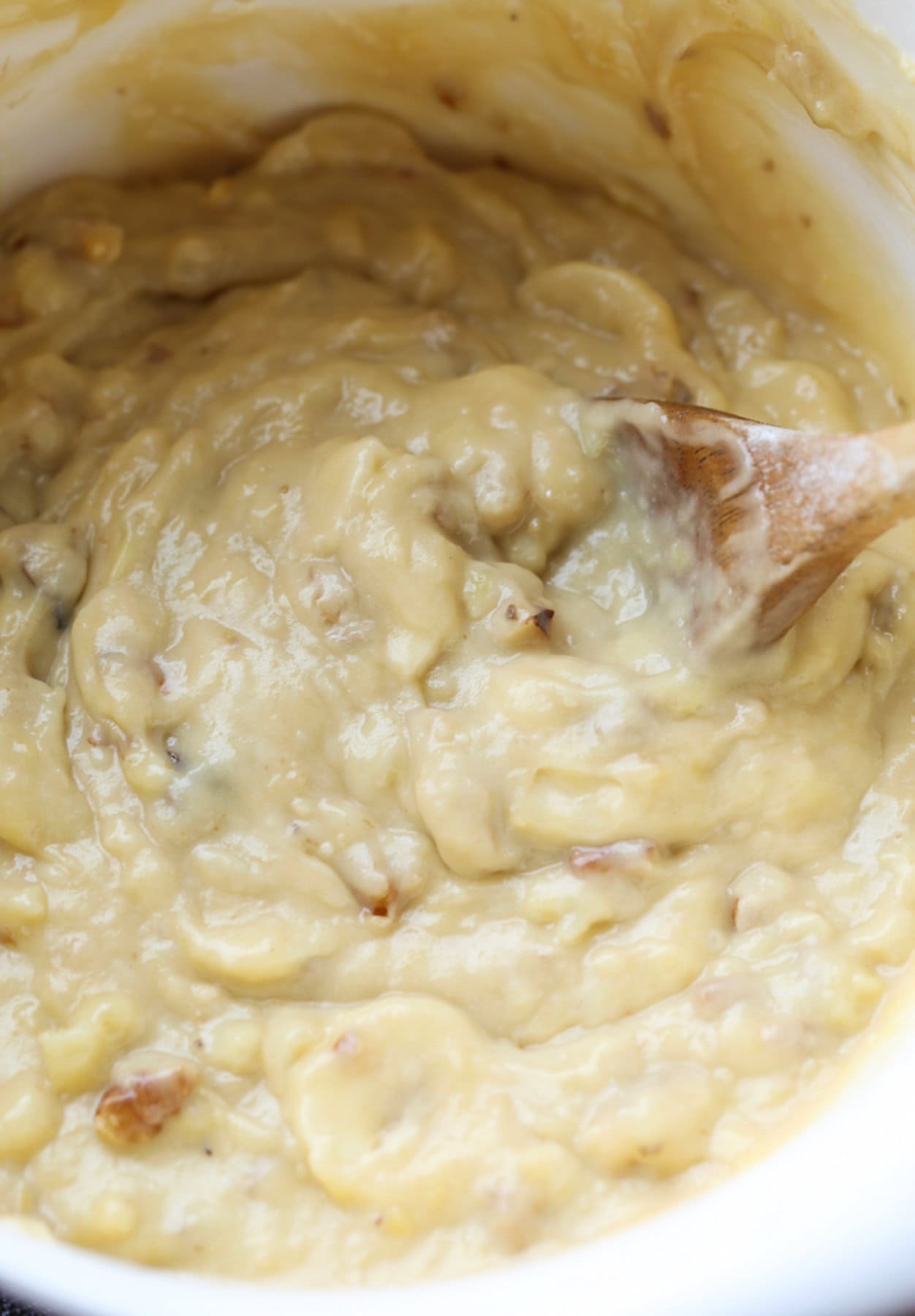 Banana muffin batter in a white bowl being stirred with a wooden spoon.