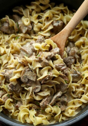 A portion of stroganoff with egg noodles being scooped out of a Crockpot with a wooden spoon.