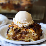 A piece of bread pudding made with day old biscuits on a white plate with vanilla ice cream.