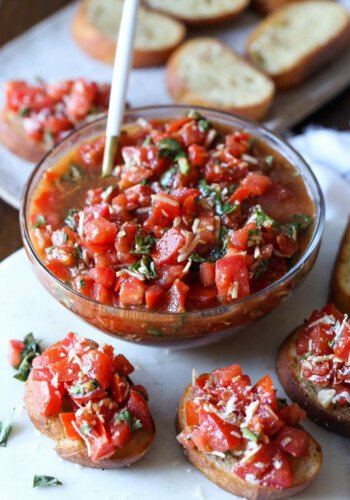 A bowl of bruschetta surrounded by bruschetta toasts.