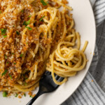 Overhead view of Caesar pasta on a white plate topped with garlic breadcrumbs and parsley, next to pasta swirled on a fork.