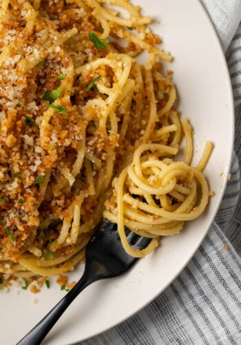 Overhead view of Caesar pasta on a white plate topped with garlic breadcrumbs and parsley, next to pasta swirled on a fork.