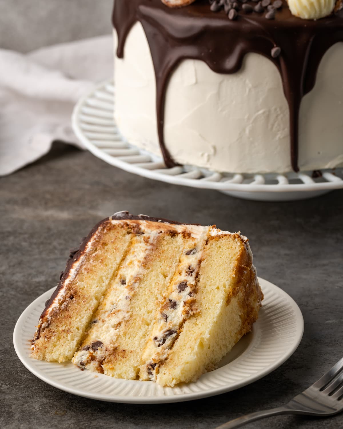 A slice of cannoli cake on a plate, with the full cake in the background.