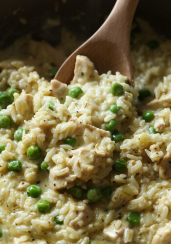 A wooden spoon is used to serve creamy chicken and rice with green peas.