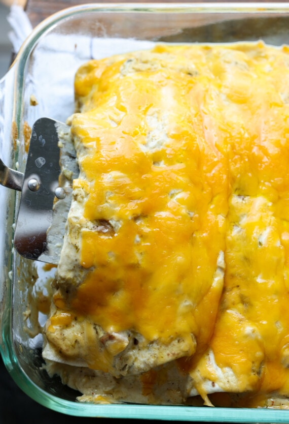 Serving cheesy chicken enchiladas in a casserole dish with a spatula