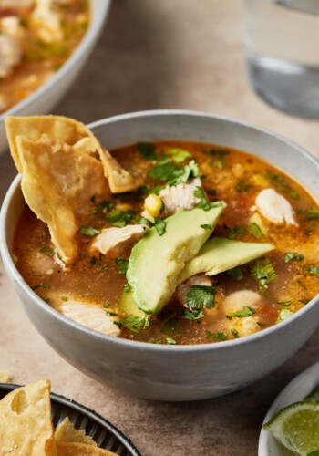 A bowl of Mexican chipotle lime chicken soup garnished with tortilla chips and avocado.