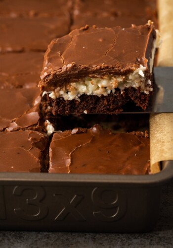 A coconut brownie is lifted from a baking pan of brownies.