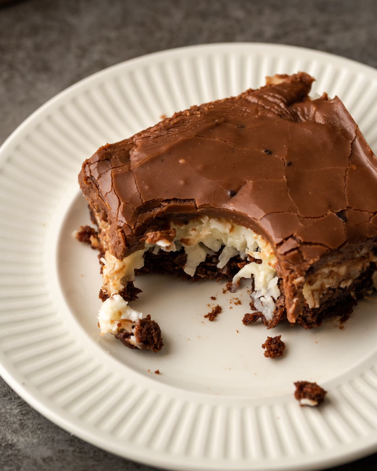 A coconut brownie with a bite missing on a white plate.