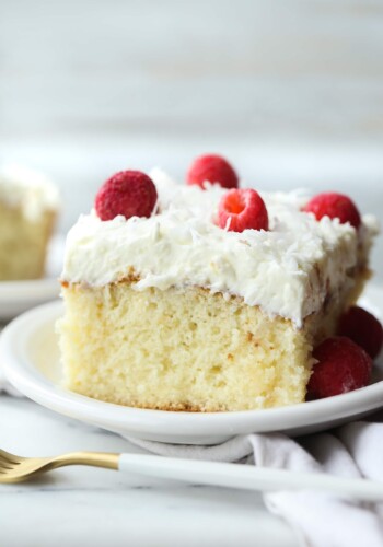 Slice of Coconut Poke Cake on a plate topped with whipped frosting