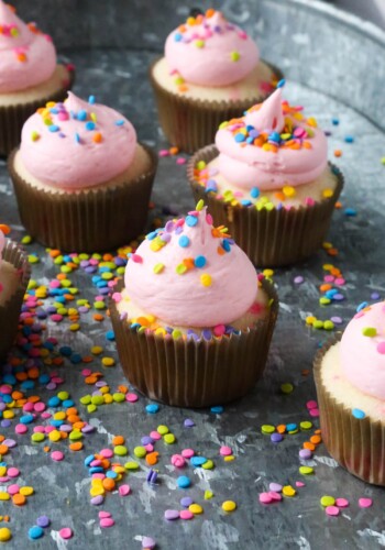 Confetti Cupcakes with pink frosting and sprinkles on top in a tray covered in sprinkles