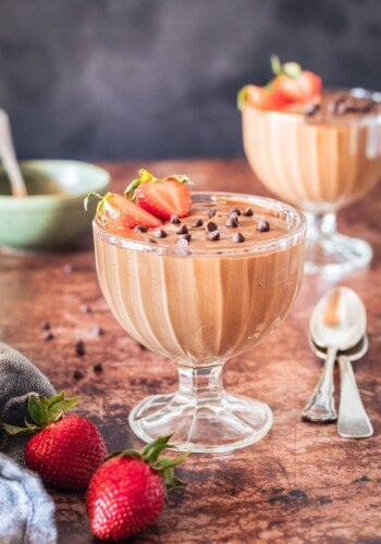 Two bowls of chocolate mousse with chocolate chips and stawberries.