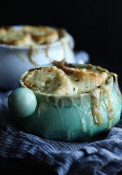 A ramekin full of French onion soup, topped with bread slices and melted Gruyere cheese.