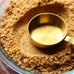 Measuring cup pressing into a graham cracker crust.