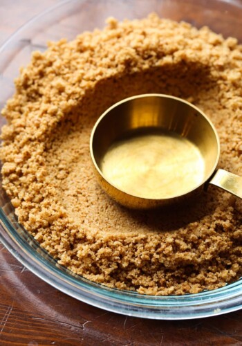 Measuring cup pressing into a graham cracker crust.