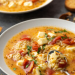 A bowl of Greek tomato feta soup with a spoon, and another bowl of soup in the background.