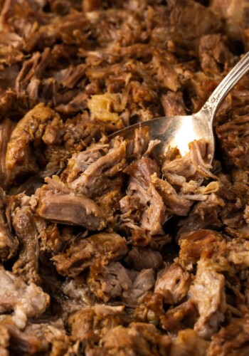 A fork stuck into Instant Pot carnitas on a metal baking sheet.