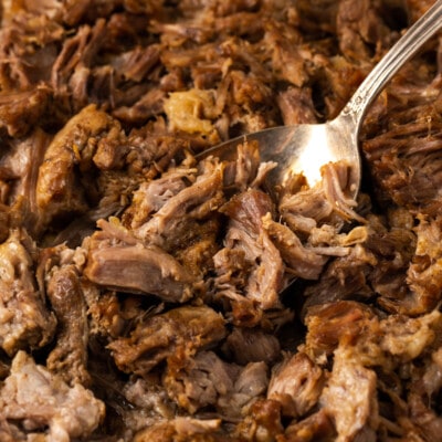 A fork stuck into Instant Pot carnitas on a metal baking sheet.