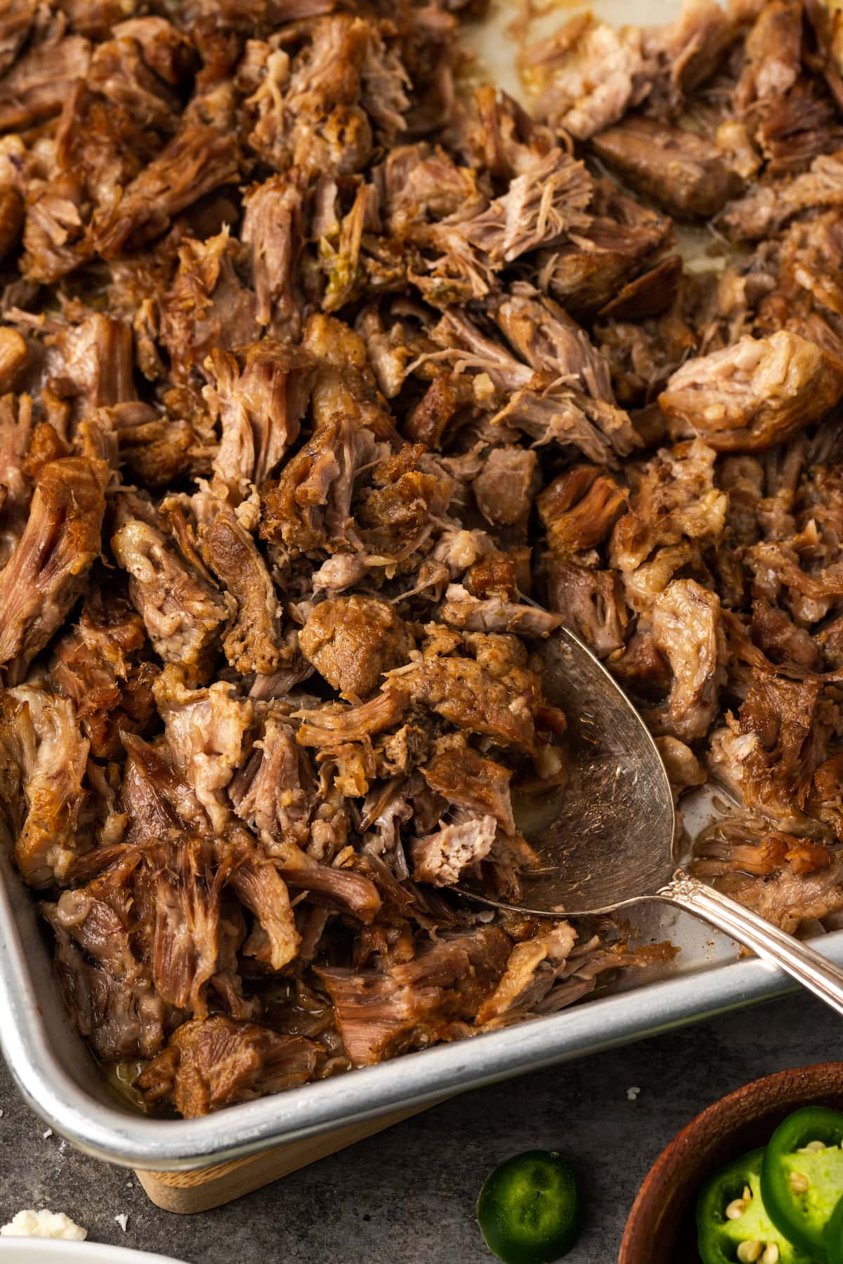 Overhead view of instant pot carnitas on a metal baking sheet with a spoon.
