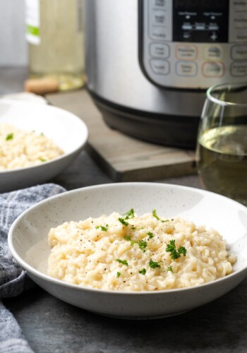 A bowl of creamy Instant Pot risotto garnished with fresh parsley, with the Instant Pot in the background.