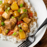 Overhead view of Instant Pot Hawaiian chicken served over rice on a white plate next to a fork.