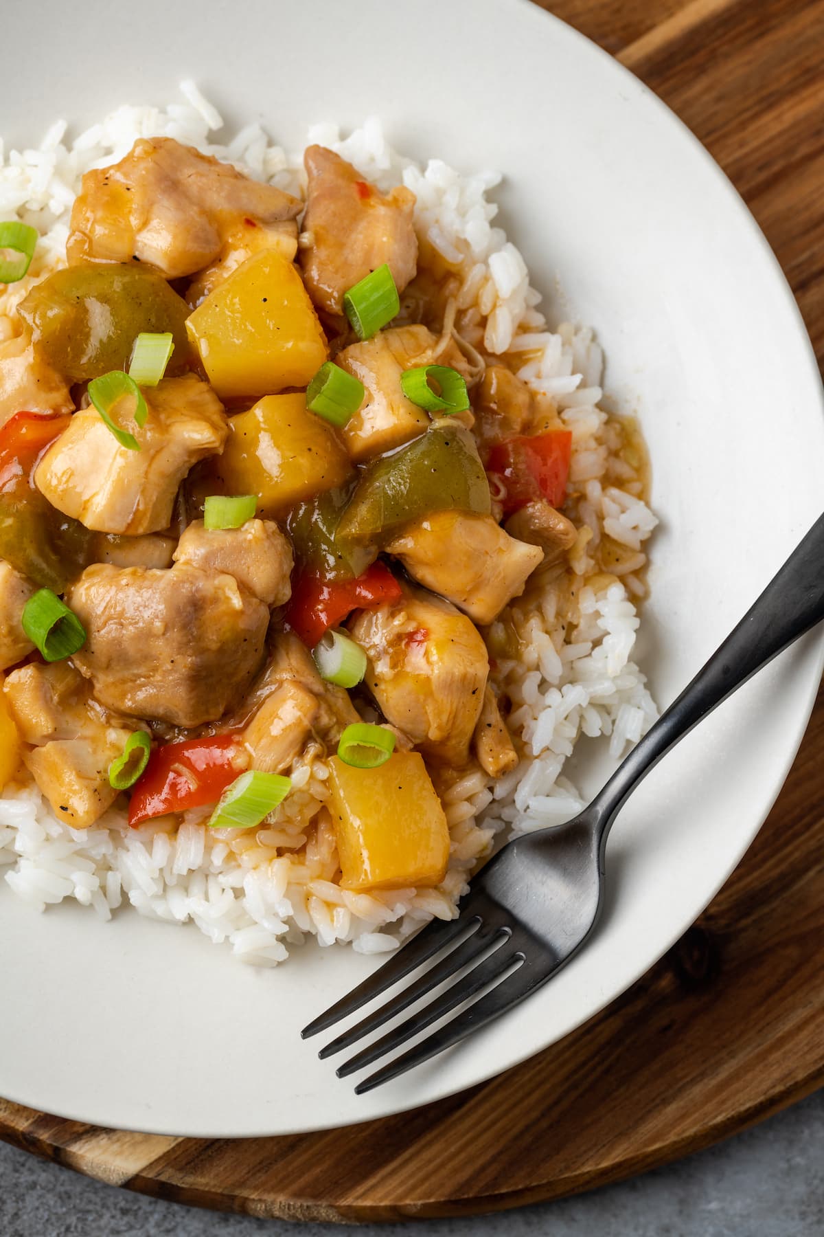 Overhead view of Instant Pot Hawaiian chicken served over rice on a white plate next to a fork.