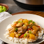 Hawaiian chicken served over rice on a white plate next to a fork, with the Instant Pot in the background.