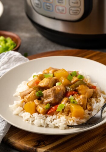 Hawaiian chicken served over rice on a white plate next to a fork, with the Instant Pot in the background.