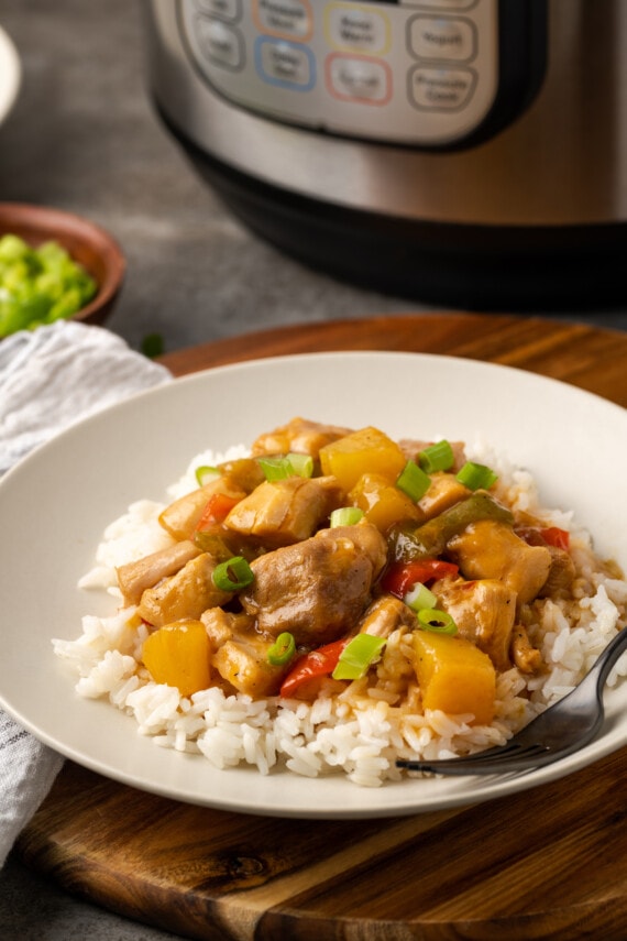 Hawaiian chicken served over rice on a white plate next to a fork, with the Instant Pot in the background.