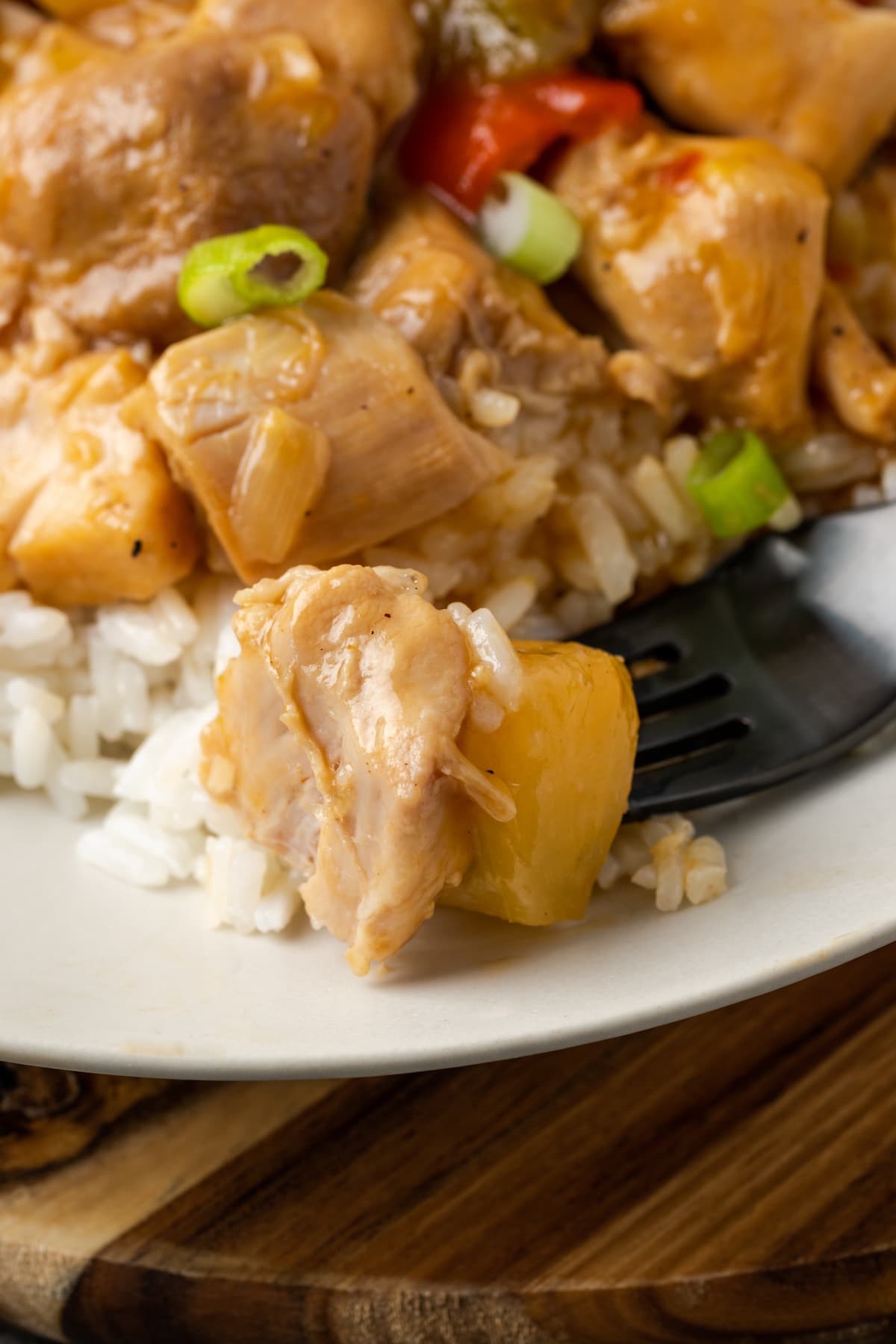 A forkful of Hawaiian chicken on a white plate next to more chicken served over rice.