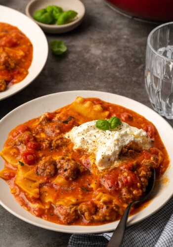 A bowl of lasagna soup topped with ricotta cheese and basil leaves.