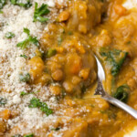 Close up view of a bowl of lentil soup topped with grated parmesan cheese, with a spoon.