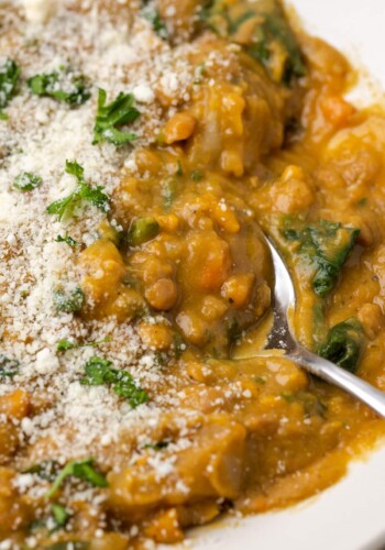 Close up view of a bowl of lentil soup topped with grated parmesan cheese, with a spoon.