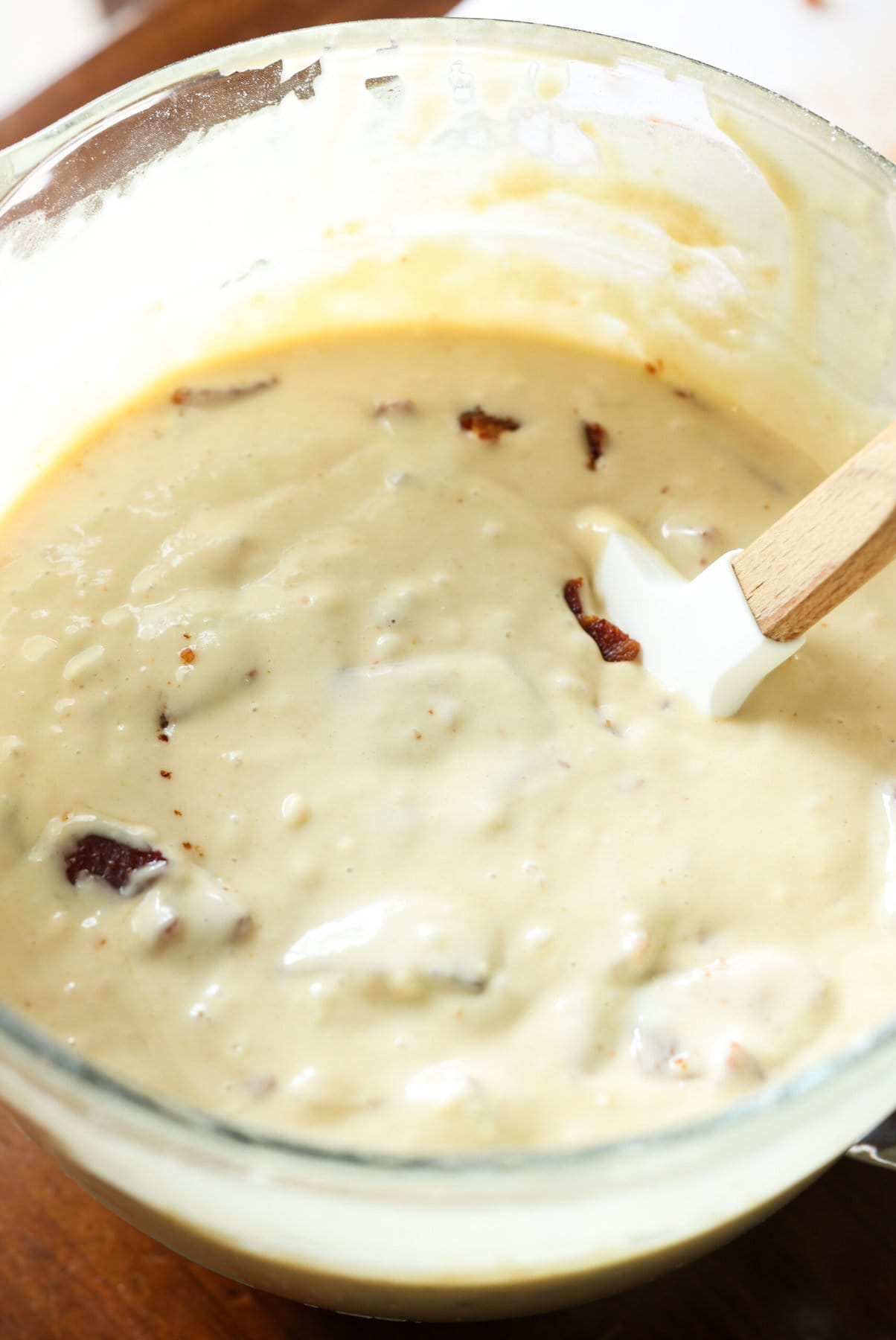 Pancake batter with a rubber spatula stirring in diced bacon