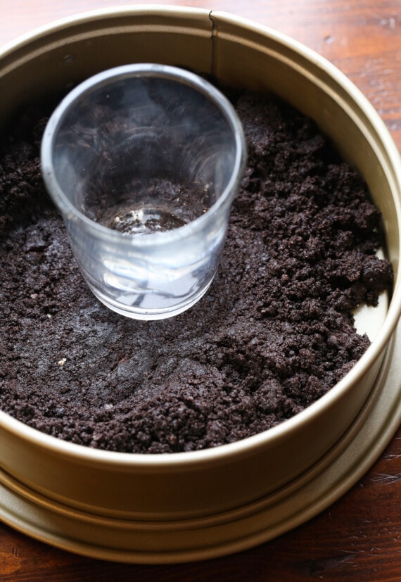 Oreo crumbs being pressed into a springform pan.