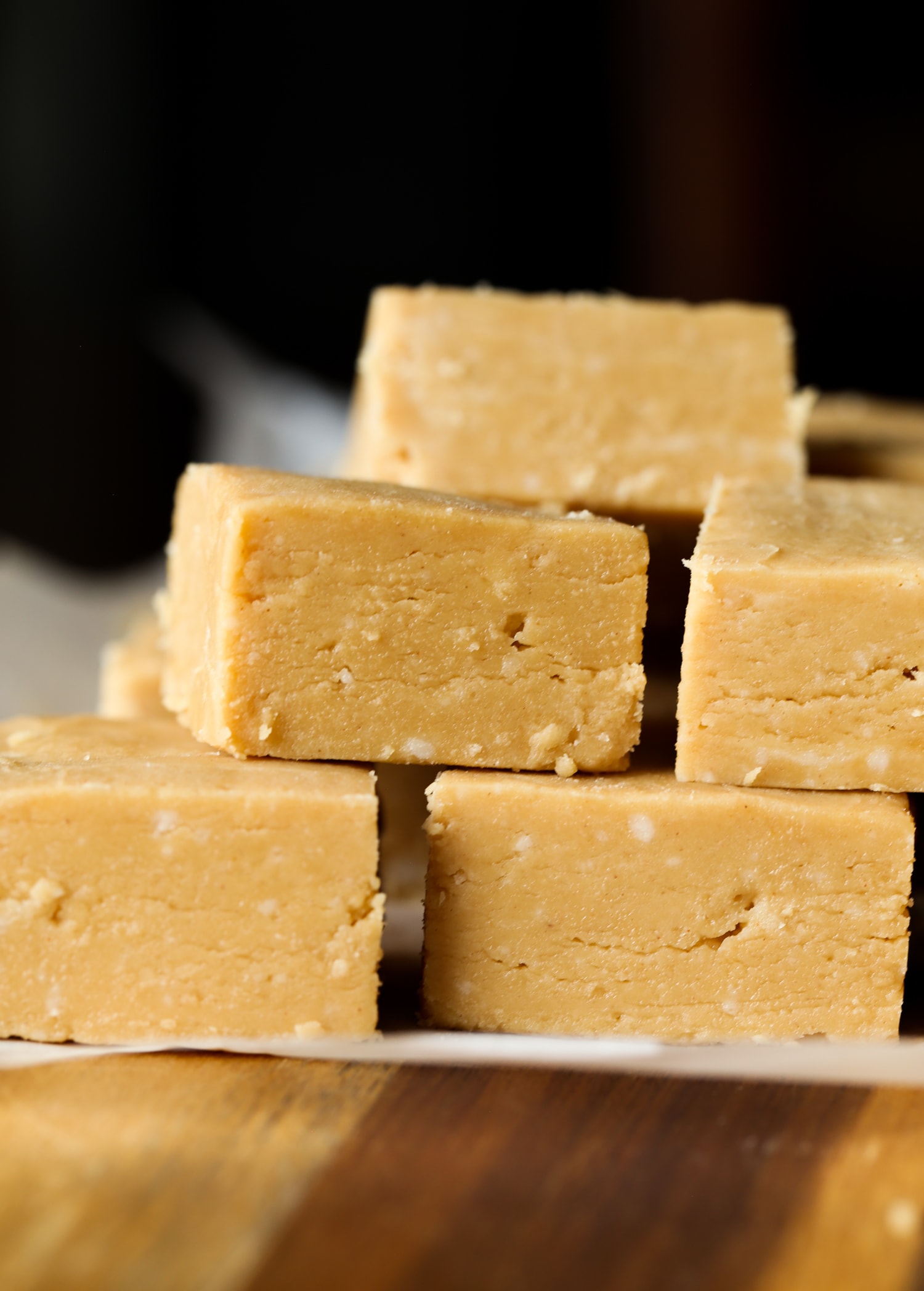 Peanut butter fudge squares stacked on top of each other on a piece of parchment paper.