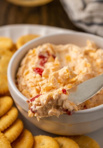 Close up of a bowl of pimento cheese served with a cheese knife on a platter of crackers.