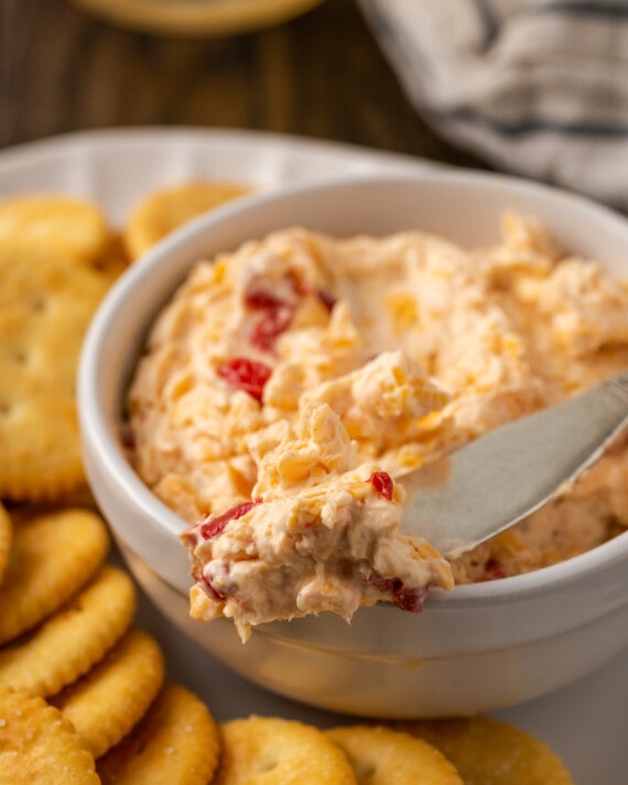 Close up of a bowl of pimento cheese served with a cheese knife on a platter of crackers.