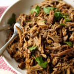 slow cooker carnitas in a shallow bowl shredded with a fork