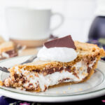 A slice of s'mores pie on a plate topped with marshmallow creme and a piece of chocolate