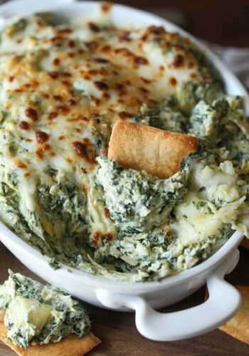 A pita chip is used to scoop creamy spinach and artichoke dip.