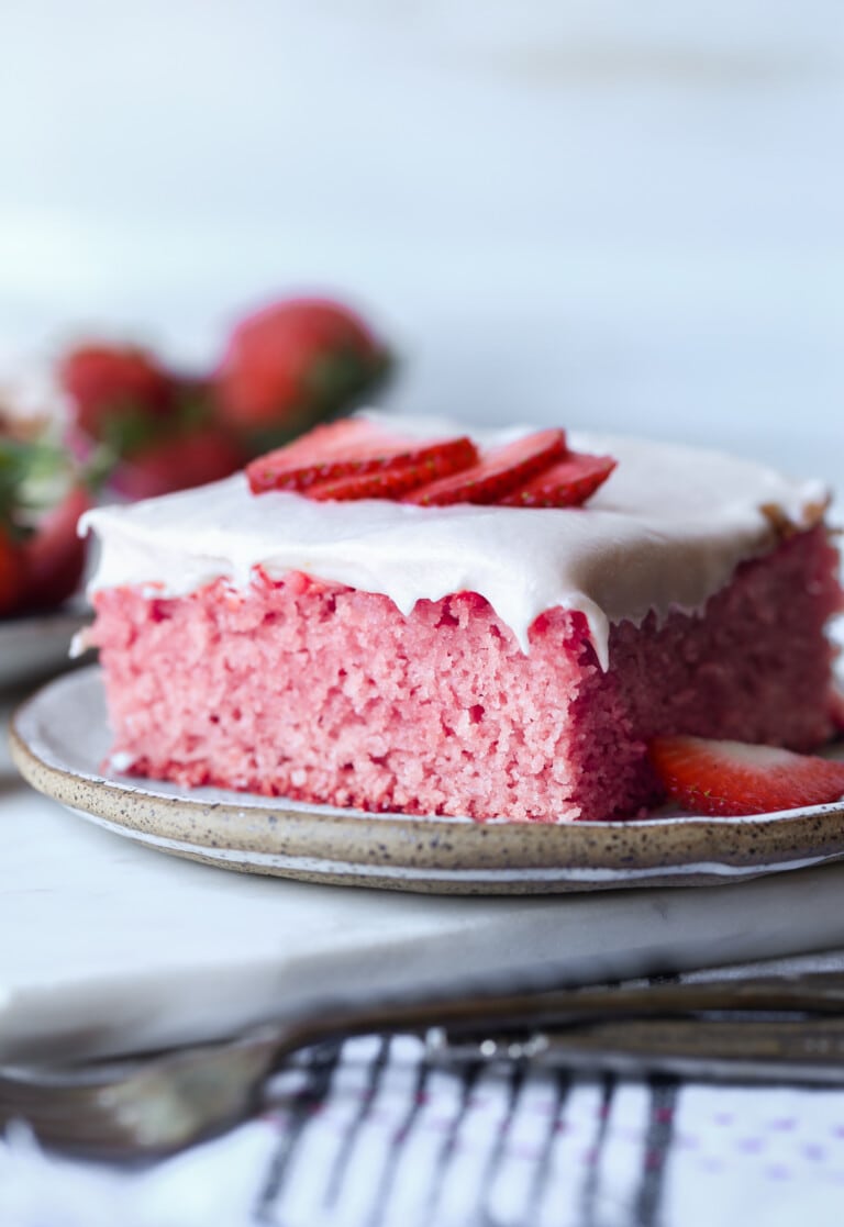 a slice of strawberry sheet cake on a plate topped with fresh strawberry slices