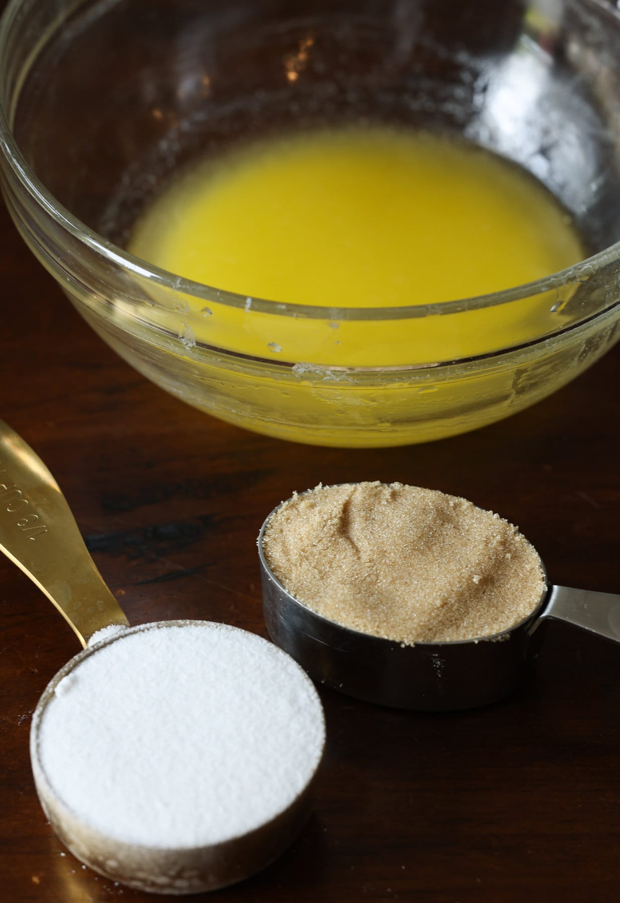 Ingredients for streusel topping on a table, the melted butter in a glass bowl, granulated sugar and light brown sugar in measuring cups