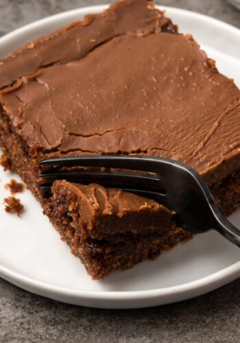 A fork cuts into a slice of chocolate sheet cake on a white plate.