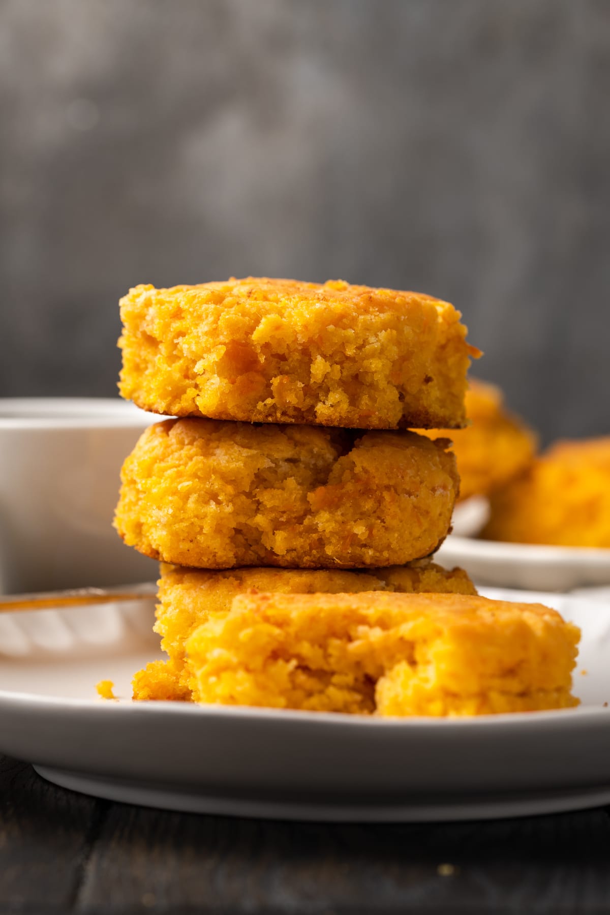 A stack of three sweet potato biscuits on a white plate, next to a fourth biscuit with a bite missing.